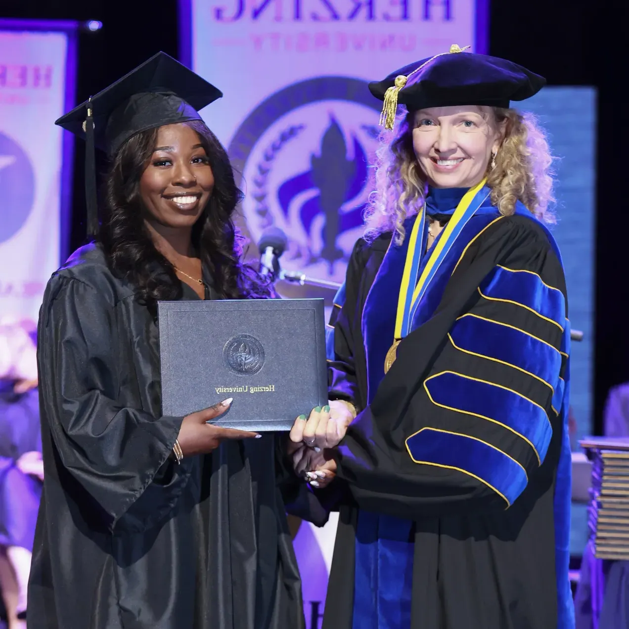 Graduate receiving a diploma on stage during a Herzing University commencement ceremony in Healthcare Administration.