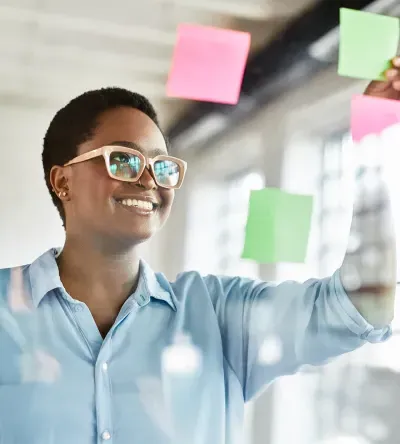 Smiling marketer placing colorful sticky notes on glass wall during brainstorming session